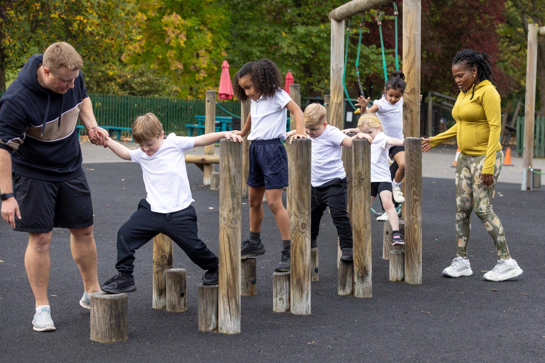 Children practicing balance on an outdoor obstacle course with teachers nearby
